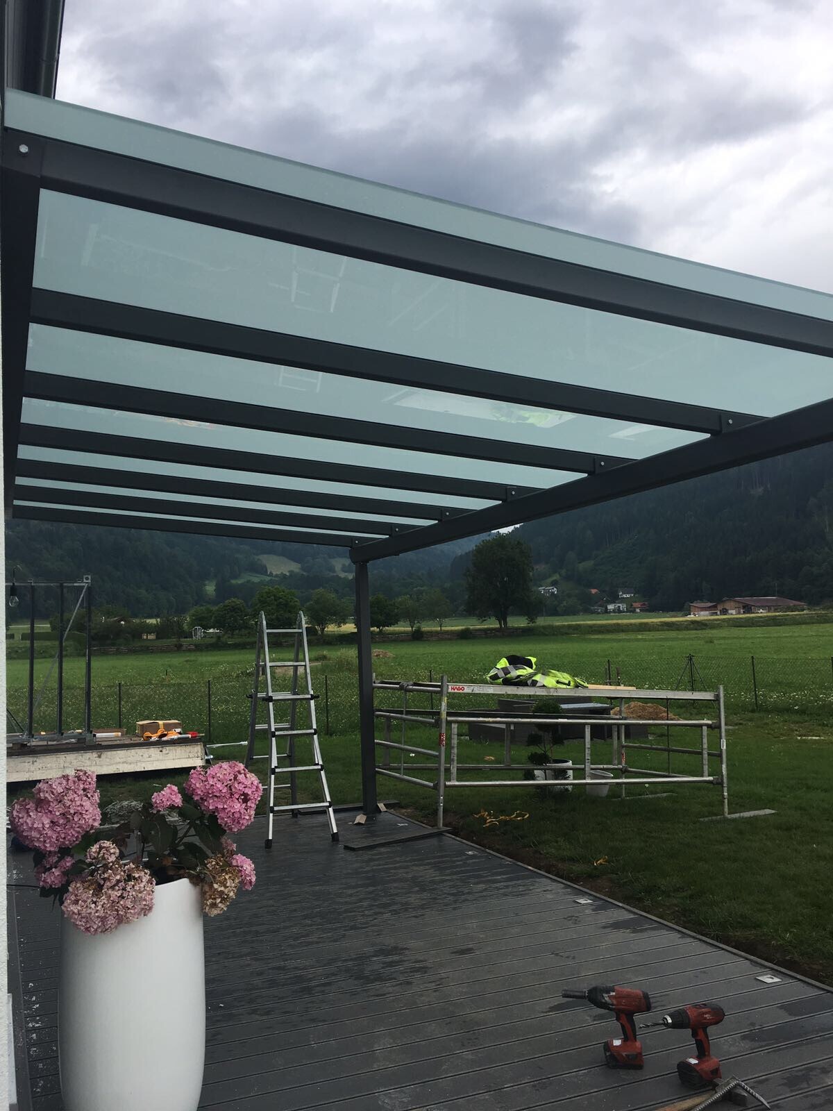 Glasüberdachung über Terrasse; Leiter, Gerüst, Werkzeuge, Topfpflanzen, ländliche Landschaft.