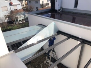 Außenbereich mit Glasdach und Stahlrahmen, Person auf Leiter vor Balkon