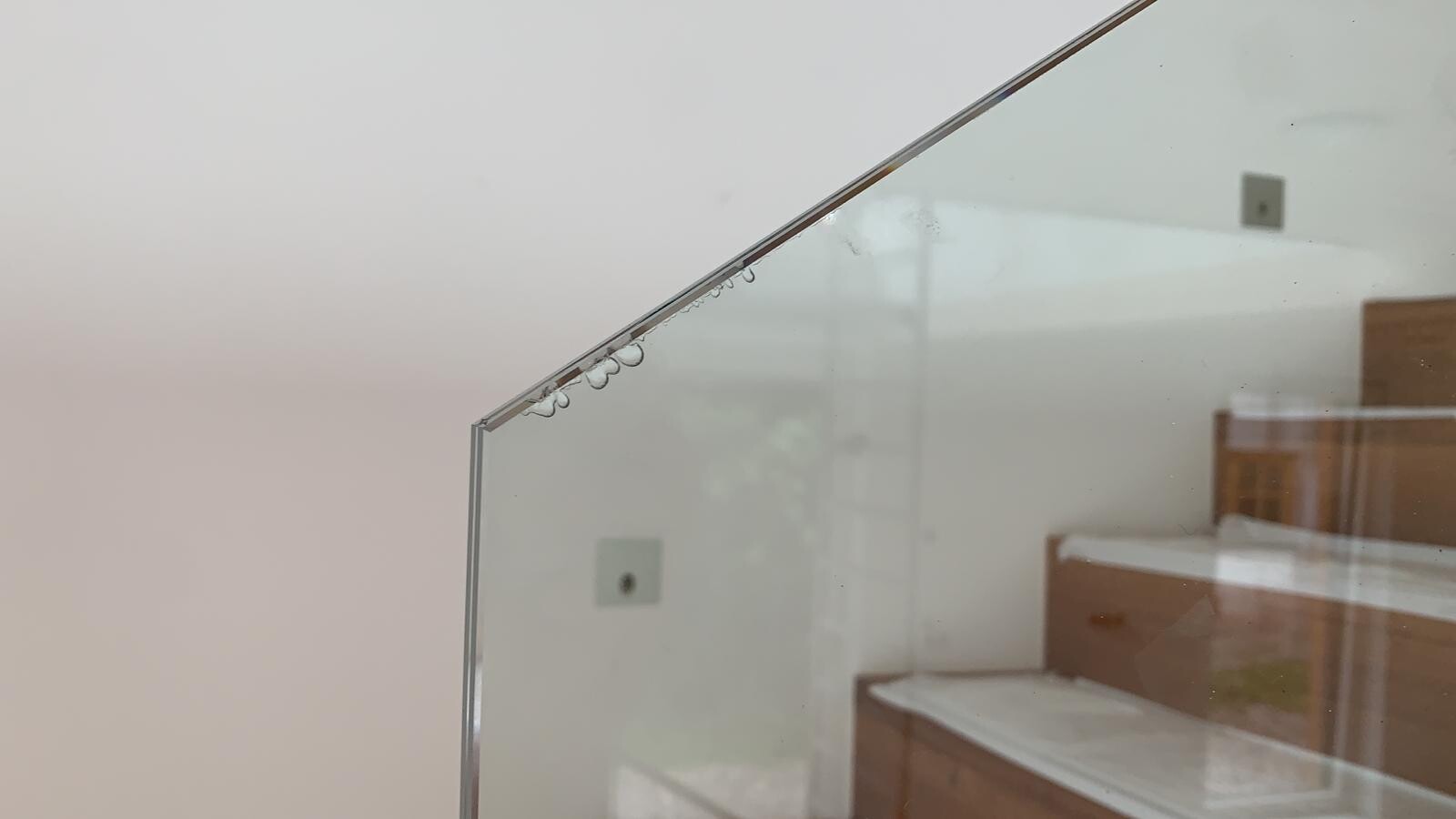 Diagonales Glaspaneel mit Wassertropfen am Rand, Blick auf Treppen im Raum