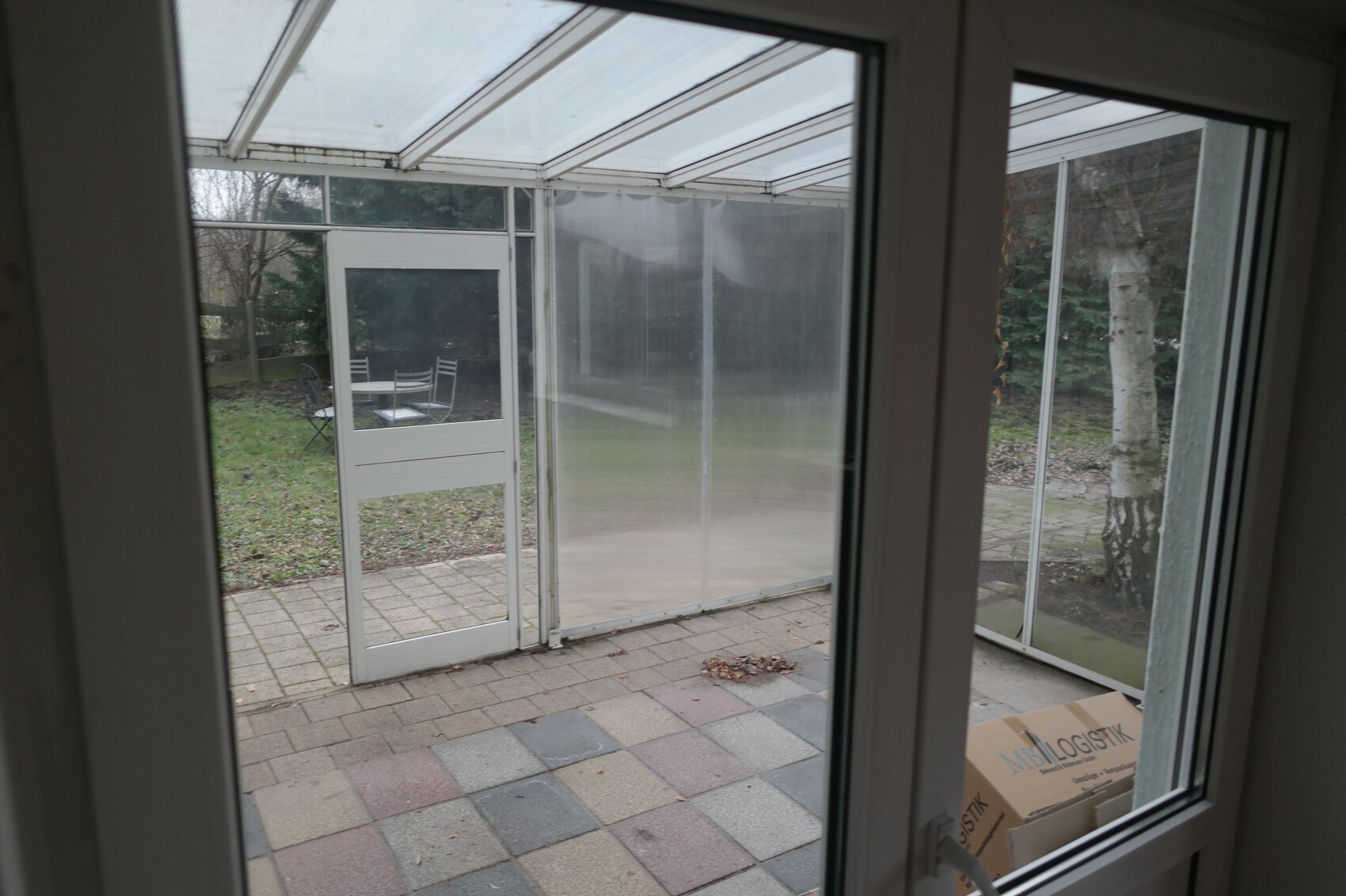 Blick durch Fenster in verglaste Veranda auf Garten mit Möbeln; Karton auf Boden