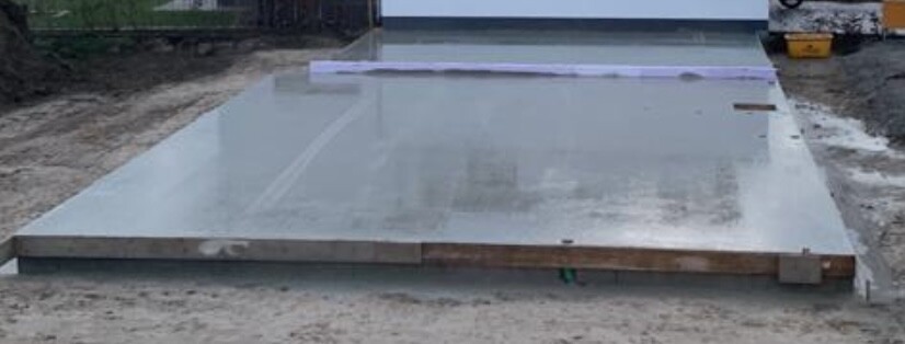 Große Stahlplatte liegt flach auf einer Baustelle, provisorisch mit Holzklötzen gestützt.