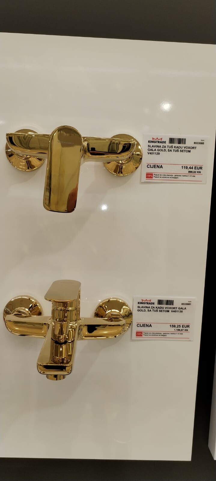 Zwei goldene Badarmaturen an einer weißen Verkaufswand mit Preisschildern.