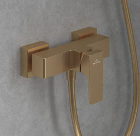 Wandmontierte goldene Badarmatur mit Schlauchbrause an grauer Wand
