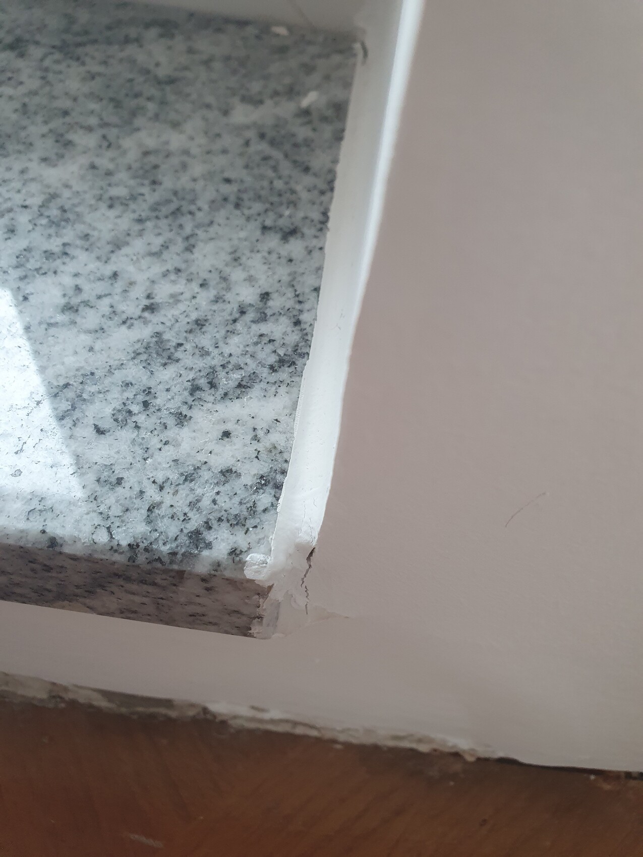 Nahaufnahme einer Granit-Küchenarbeitsplatte mit beschädigter Kantenverkleidung neben der Wand
