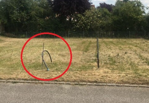 Grünfläche am Grundstück mit Zaunpfahl und losem Kabel am Straßenrand