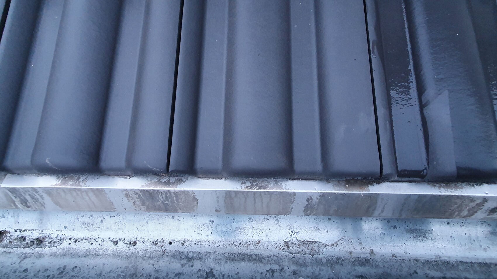 Nahaufnahme dunkler Metall-Dachbleche mit vertikalen Rippen und schmutzigem Rand