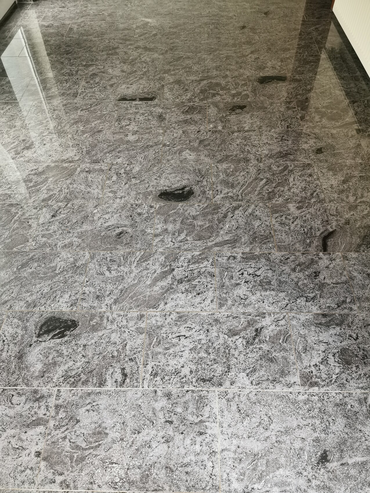 Grauer Marmoreffekt-Fliesenboden mit dunklen Flecken und Glanzreflexen.