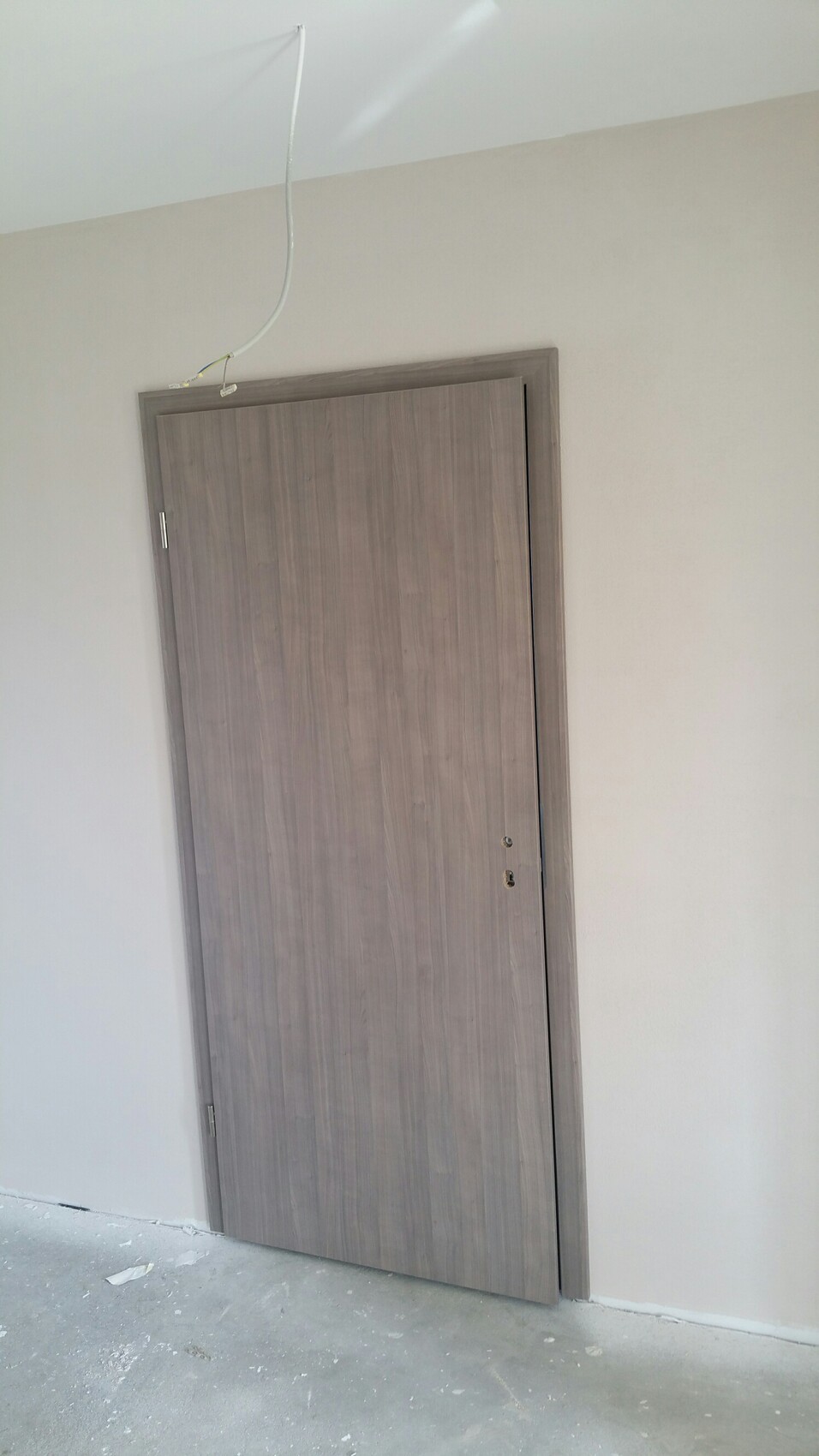 Graue Holztür vor hellem Raum; lose Kabel von der Decke hängt; Baustellenszene.