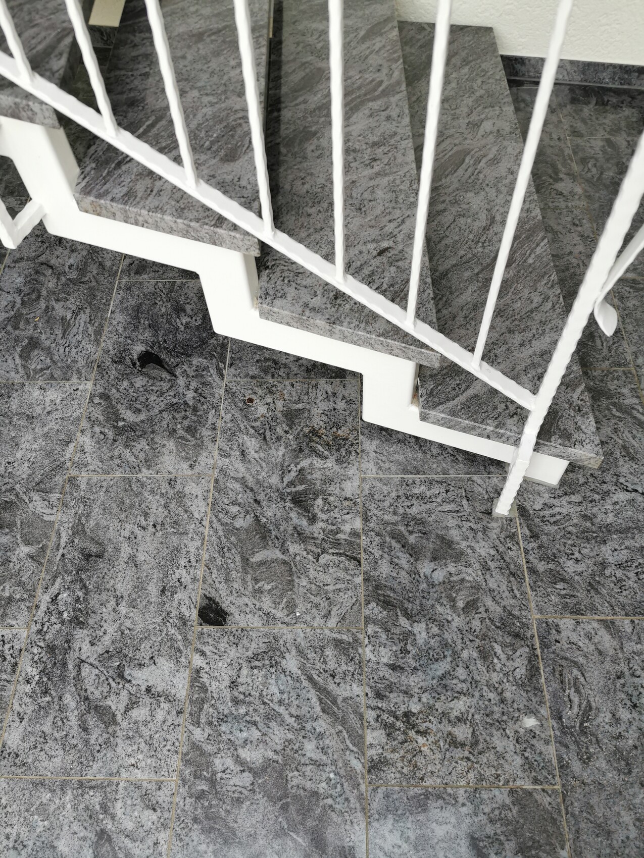 Aufsicht über eine graue Stein-Stufen-Treppe mit weißem Geländer in Innenraum.