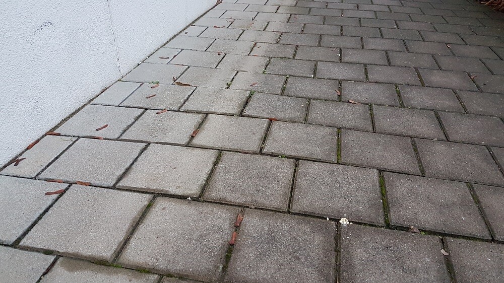 Gepflasterter Vorplatz aus grauen Pflastersteinen neben einer weißen Gebäudemauer