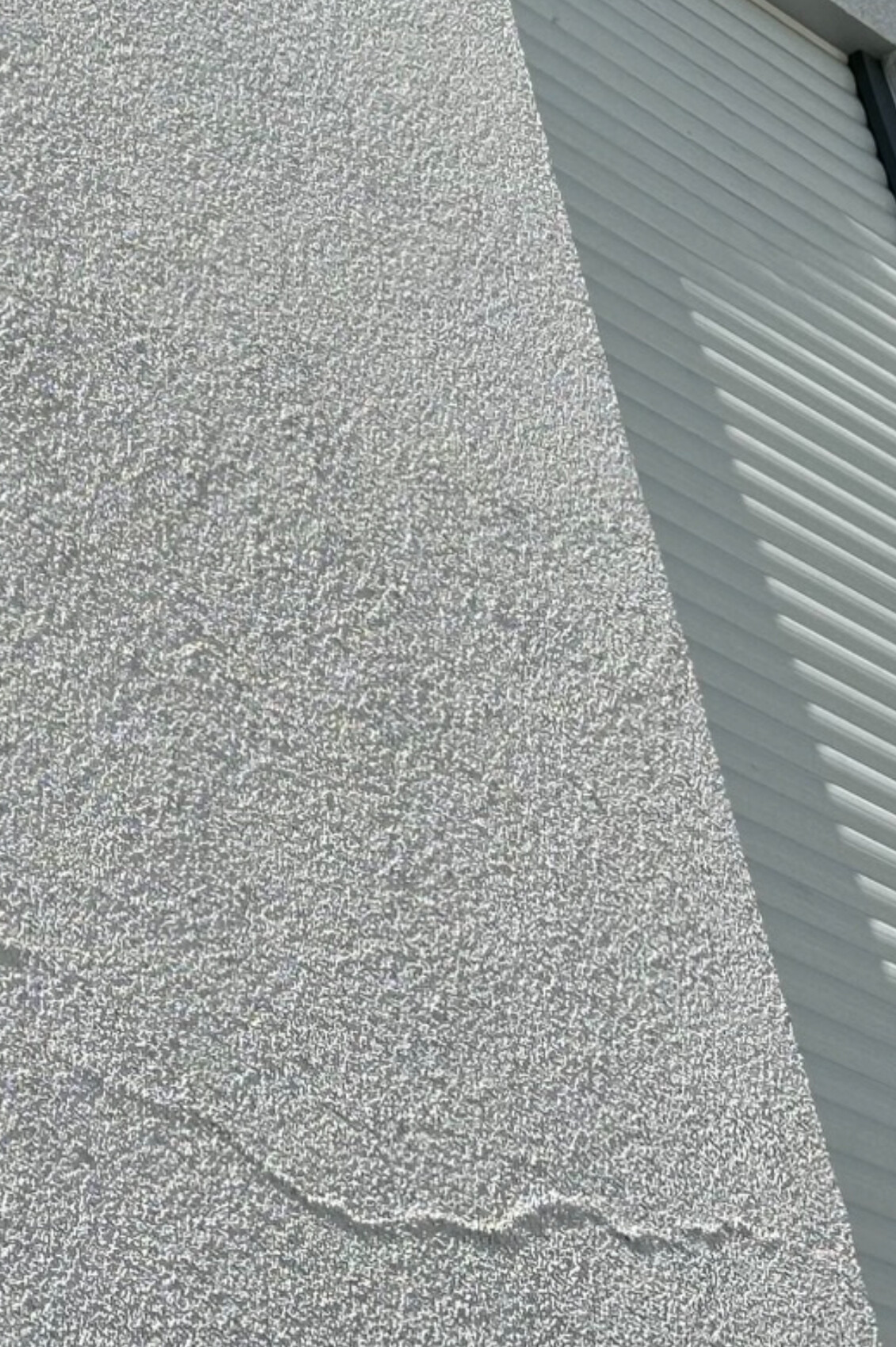 Grob strukturierte graue Wand links, rechts helle gerippte Metalloberfläche, diagonal abgegrenzt.