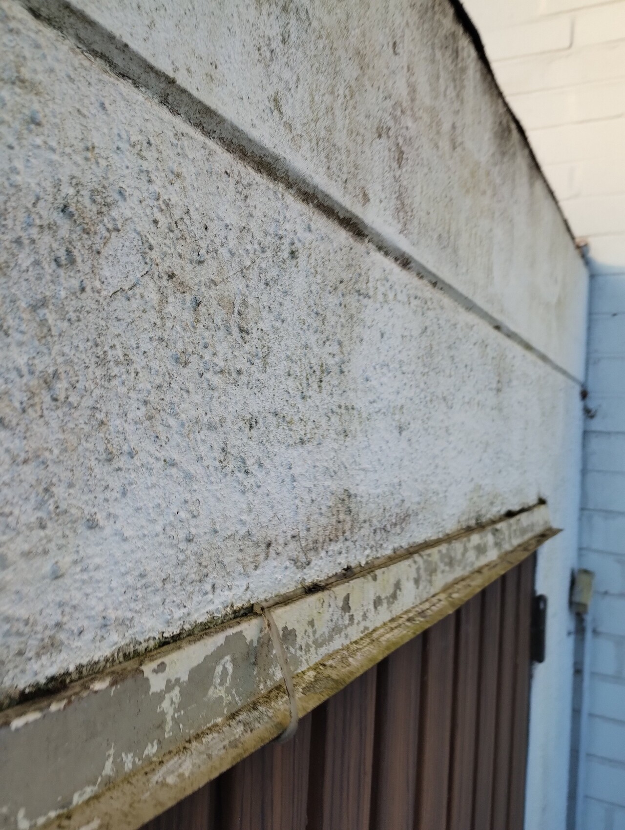 Grobe verputzte Außenwand mit horizontaler Fuge; darunter abblätternder Putz auf Holzverschlag.