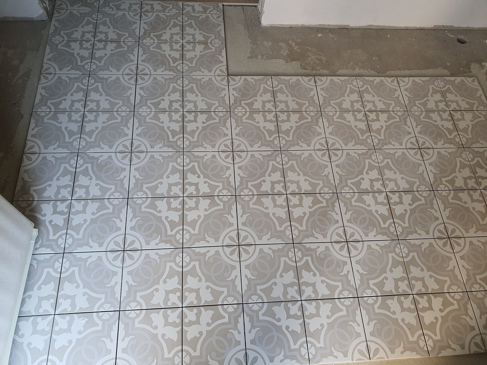 Grauer Fliesenboden mit weißem geometrischem Muster aus Kreisen und Blattformen.