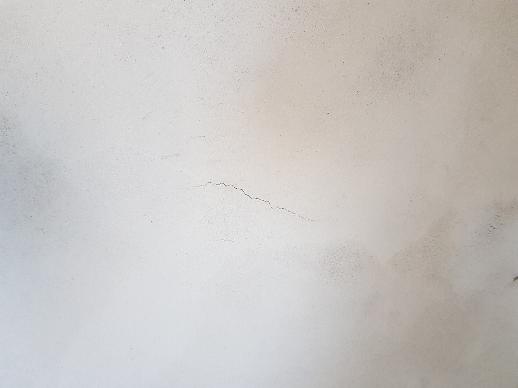 Hellgraue Betonwand mit einer feinen Rissspur in der Bildmitte