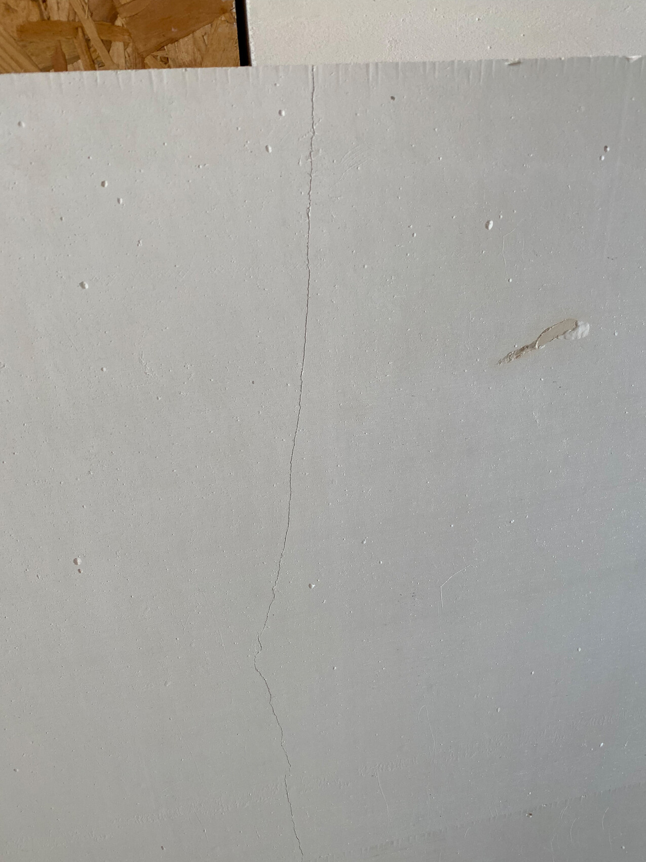 Grau verputzte Wand mit einer langen senkrechten Risslinie und kleinen Unebenheiten.