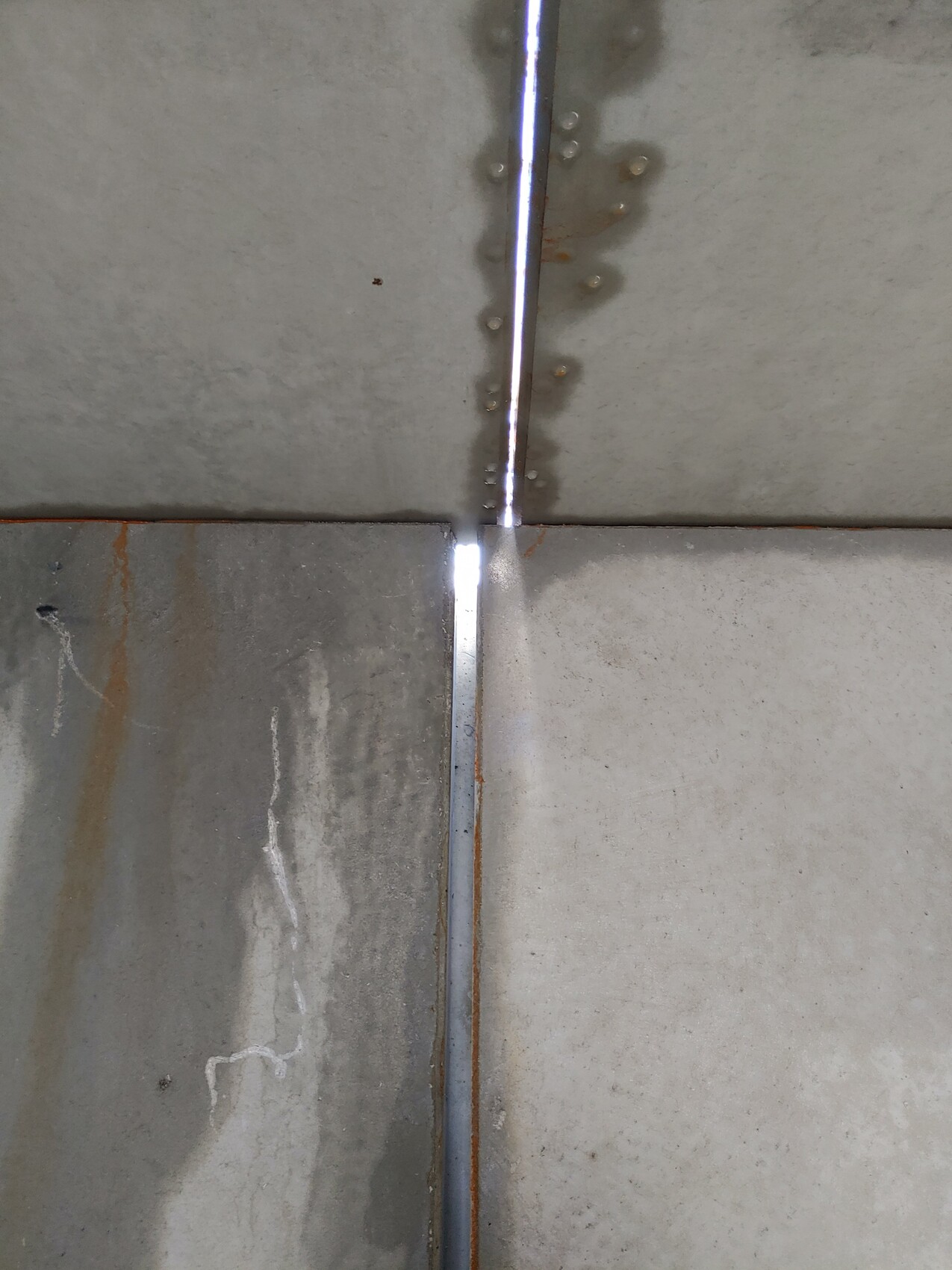 Vertikale Metallfuge zwischen Betonplatten mit Rostflecken und hellem Licht im Spalt.