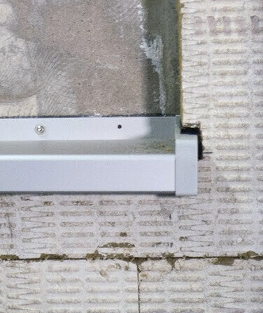Nahaufnahme einer grauen Metall-Dachkante mit Montageblech über Ziegelwand.