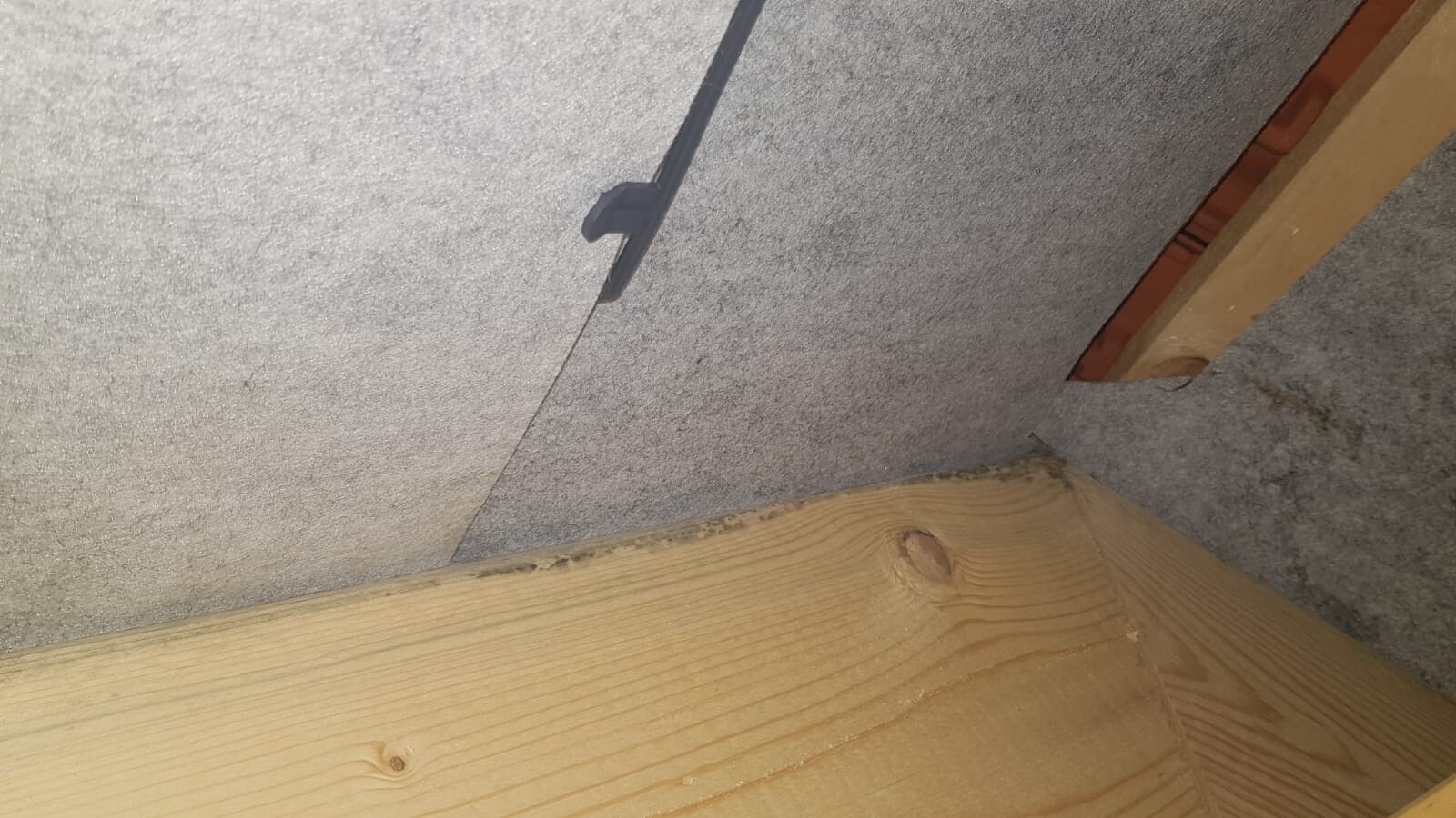 Dachboden-Ecke mit grauer Dämmplatte, Holzbalken und Kabelstrang.