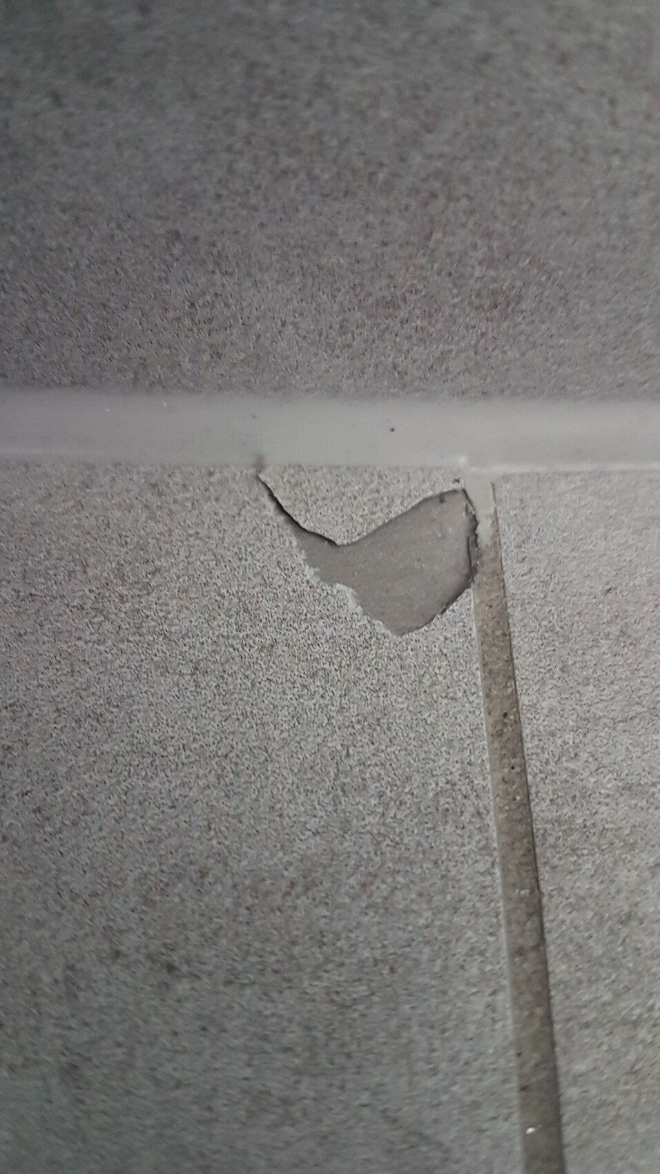 Nahaufnahme einer grauen Betonoberfläche mit abgebrochener Ecke an einer Fuge.