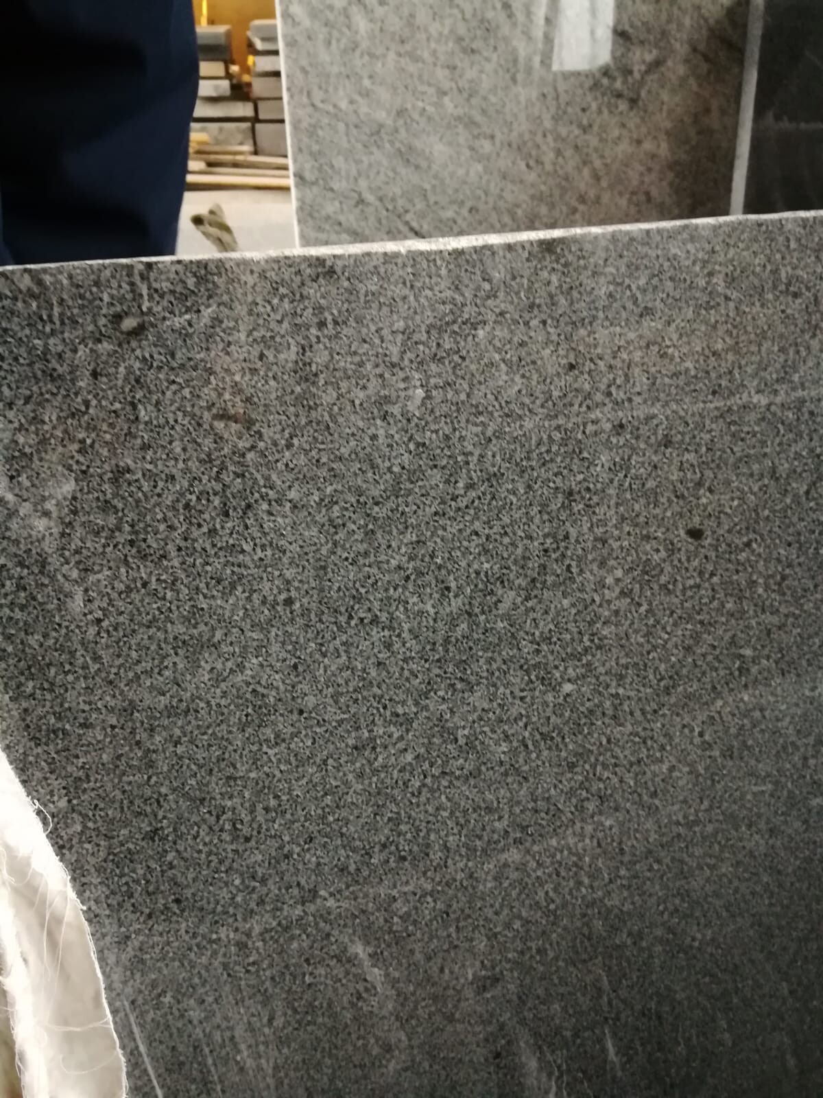 Große graue Granitplatte in Werkstatt, grobe Textur, Hintergrund mit Werkstattmaterialien.