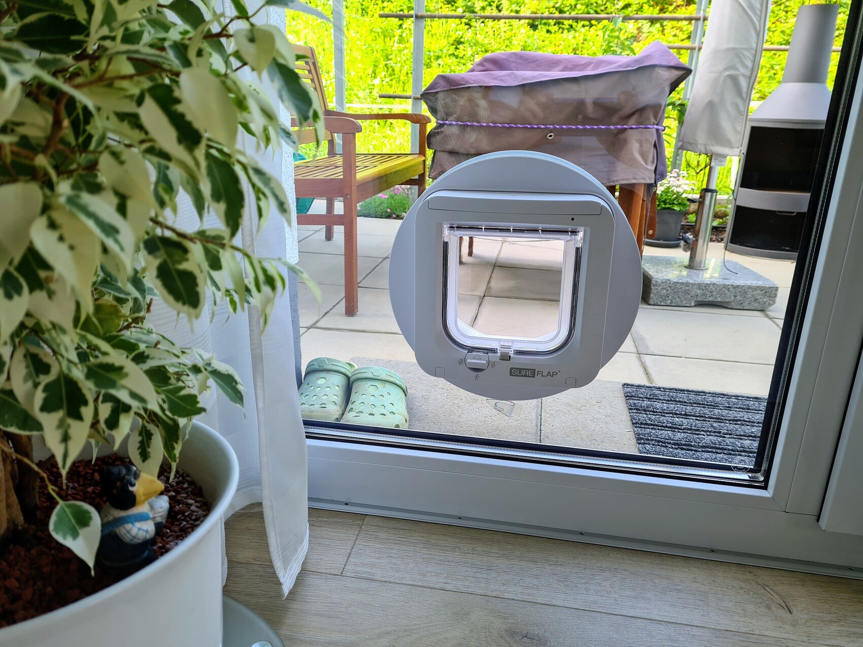 Runde Haustierklappe in Glasschiebetür; Blick nach Terrasse mit Gartenmöbeln.