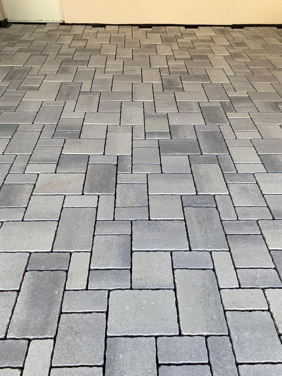 Gepflasterte Fläche aus grauen rechteckigen Pflastersteinen mit Wand im Hintergrund.