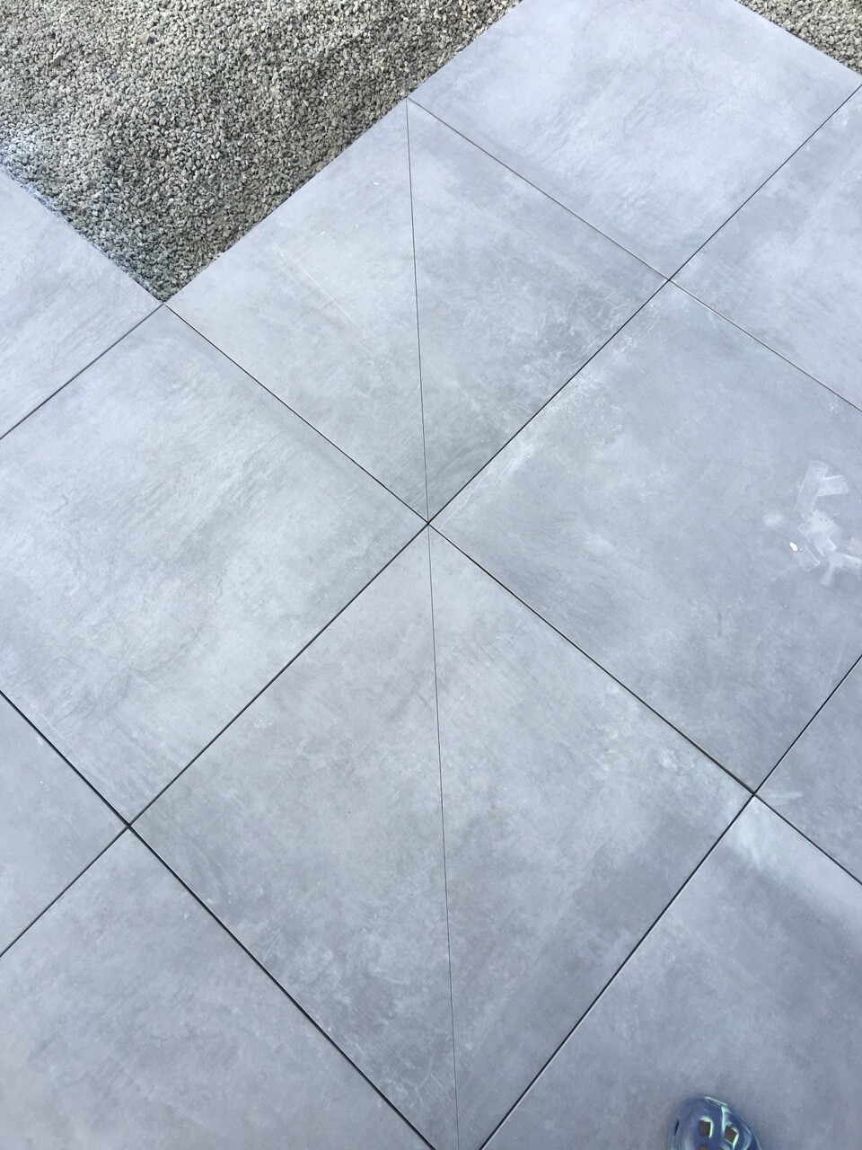 Grau quadratische Bodenplatten in diagonaler Anordnung; Kiesfläche oben, Schuh unten rechts.