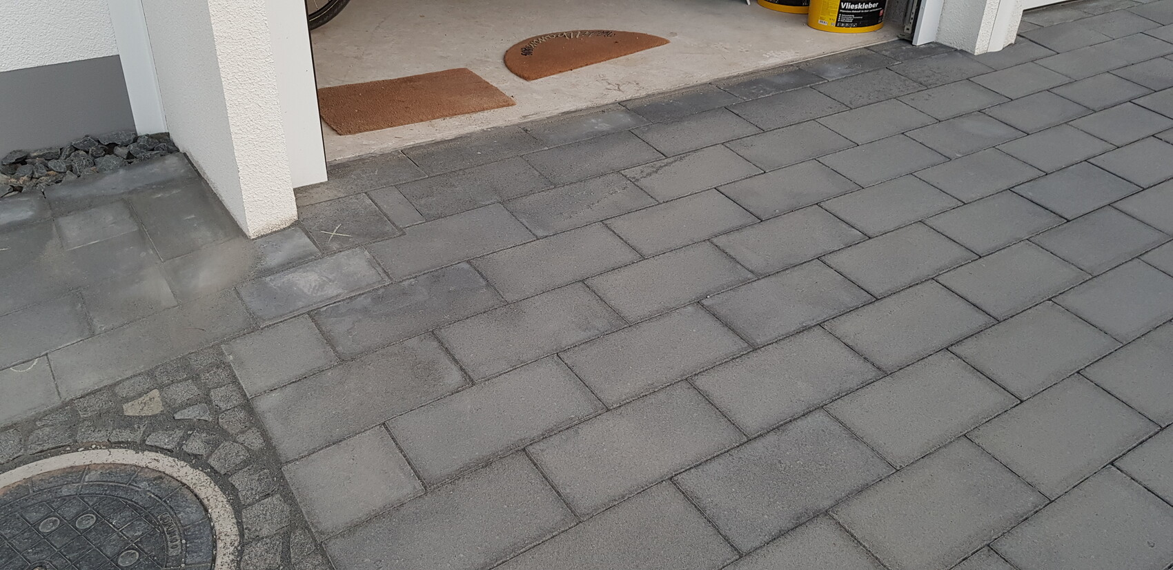 Gepflasterter Eingangsbereich vor der Garage mit grauen Pflastersteinen; zwei braune Fußmatten.