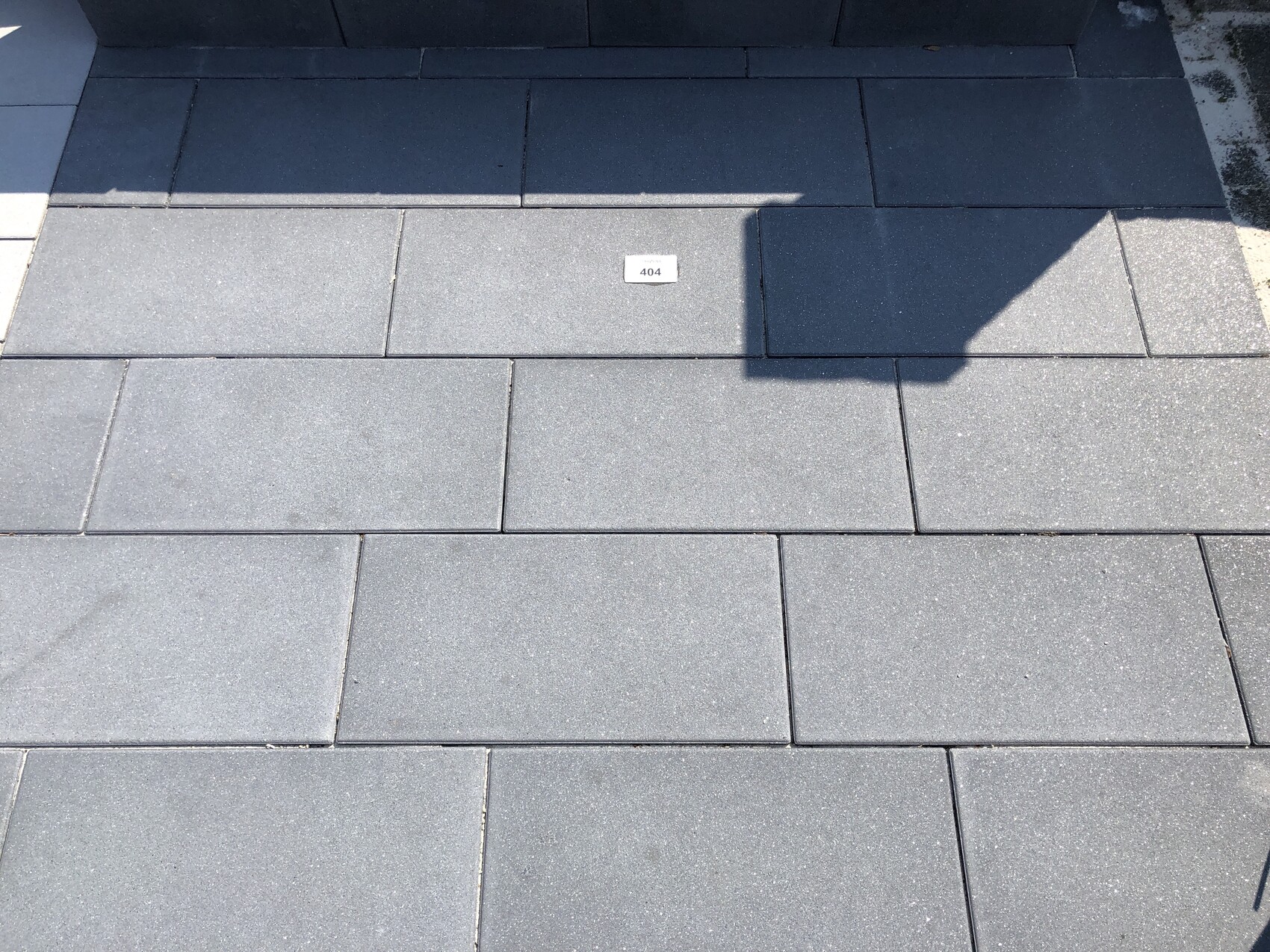 Dunkelgraue rechteckige Pflasterplatten; mittig kleines Schild mit 404, Schatten rechts.