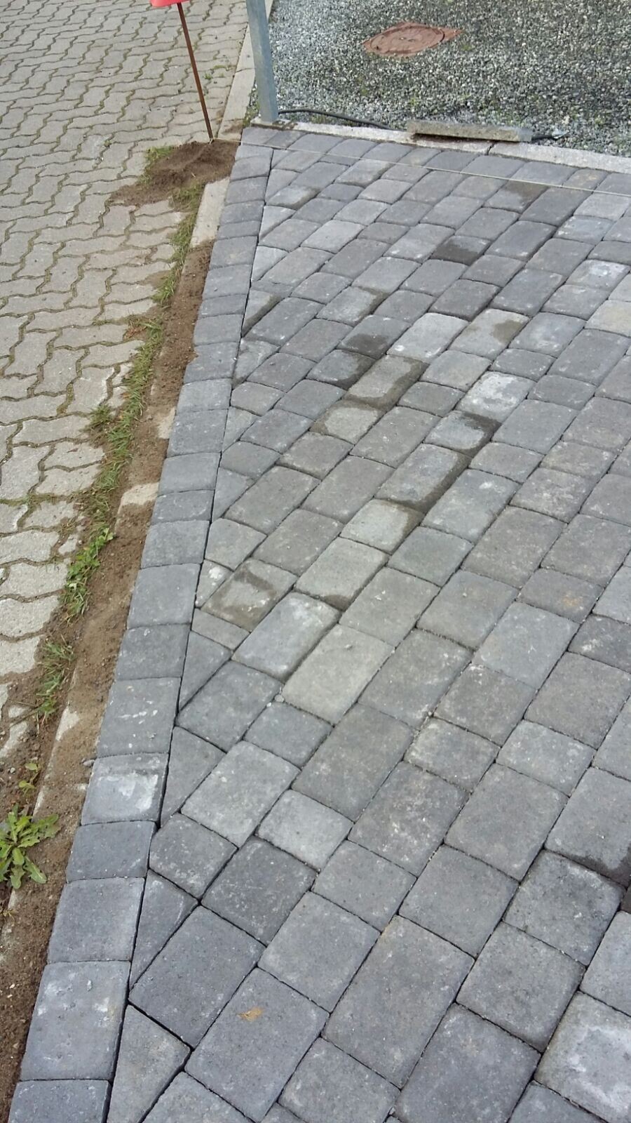 Gepflasterte Fläche aus grauen Betonsteinen, diagonal angeordnet, Randstreifen aus Erde.