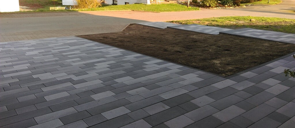 Gepflasterte Terrasse mit grauen Platten; in der Mitte ein rechteckiger Erdstreifen ohne Bepflanzung.