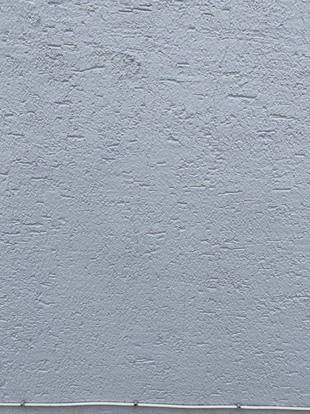 Grau verputzte Wand mit rauer Struktur und einem Rohr am unteren Rand.