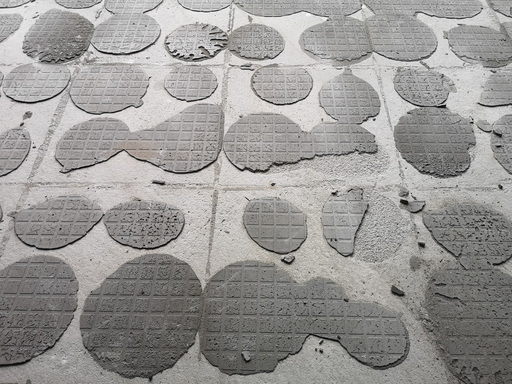 Boden mit vielen runden grauen Pflasterplatten mit Gittermuster, teils beschädigt.
