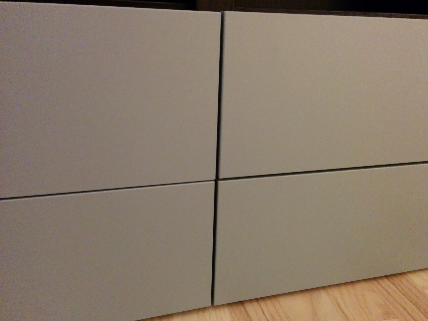 Vier graue, grifflose Schrankfronten in einer 2x2-Anordnung; Holzfußboden unten rechts sichtbar.