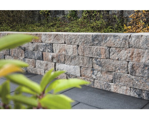 Stützmauer aus grauen Granitquadern neben dunkler Bodenfläche; grüne Blätter im Vordergrund.