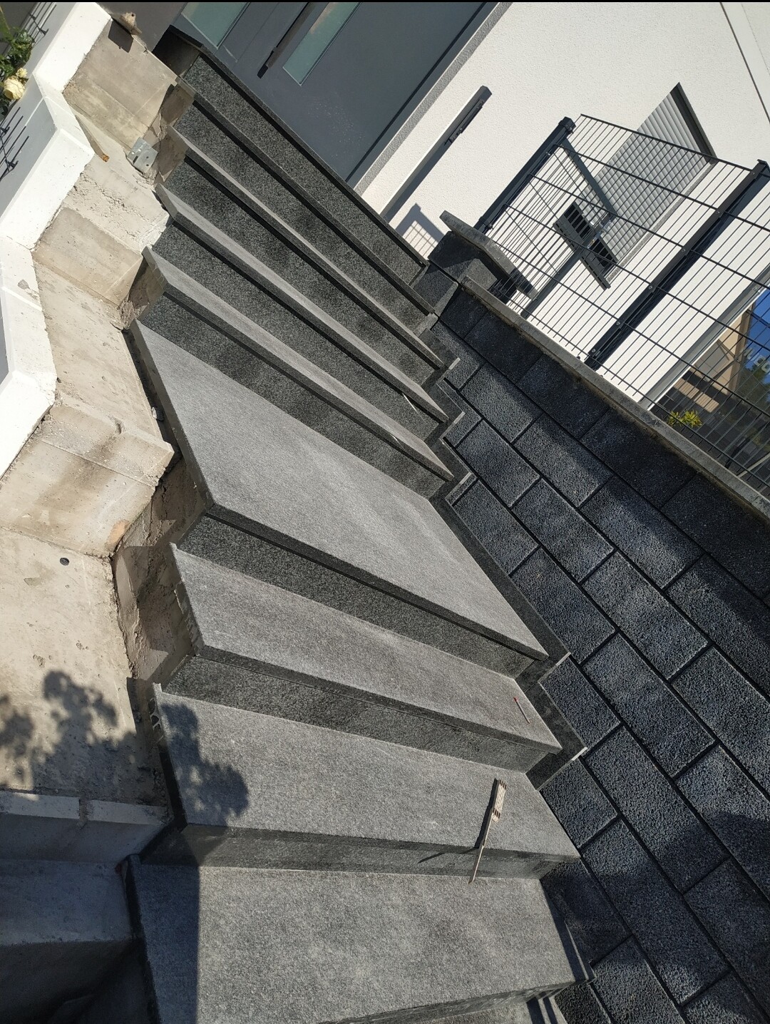 Außentreppe aus grauen Steinplatten neben moderner Gebäudefassade mit Glasfenstern und Metallzaun.