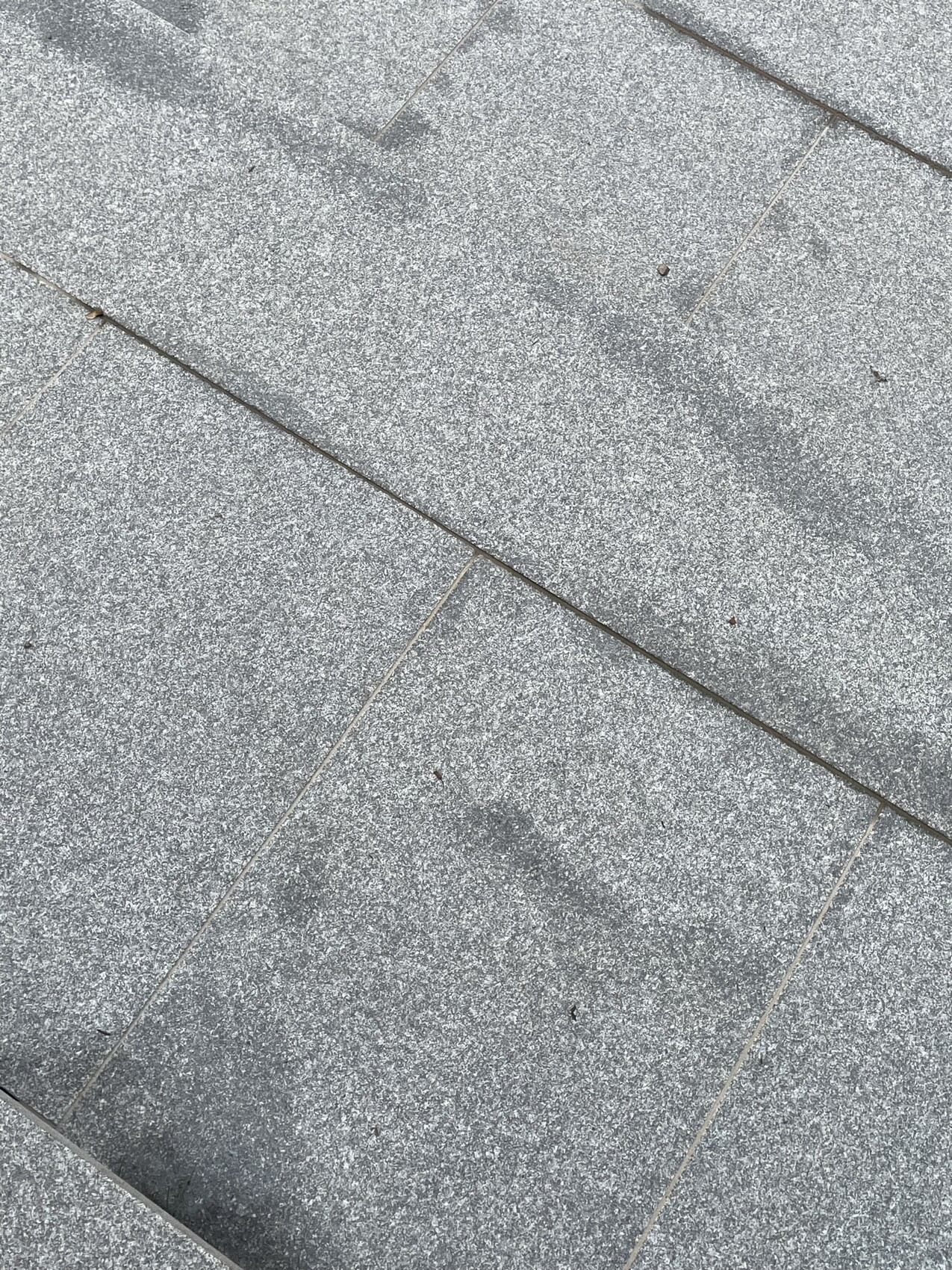 Graue Steinplatten auf Gehweg mit diagonalen Fugenlinien.