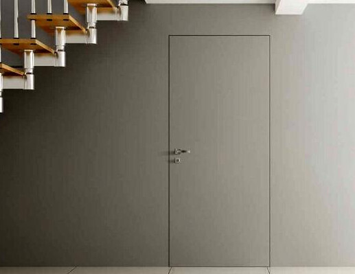 Graue Innenwand mit Tür in der Mitte; linke Treppe aus Holz und Metallstützen.