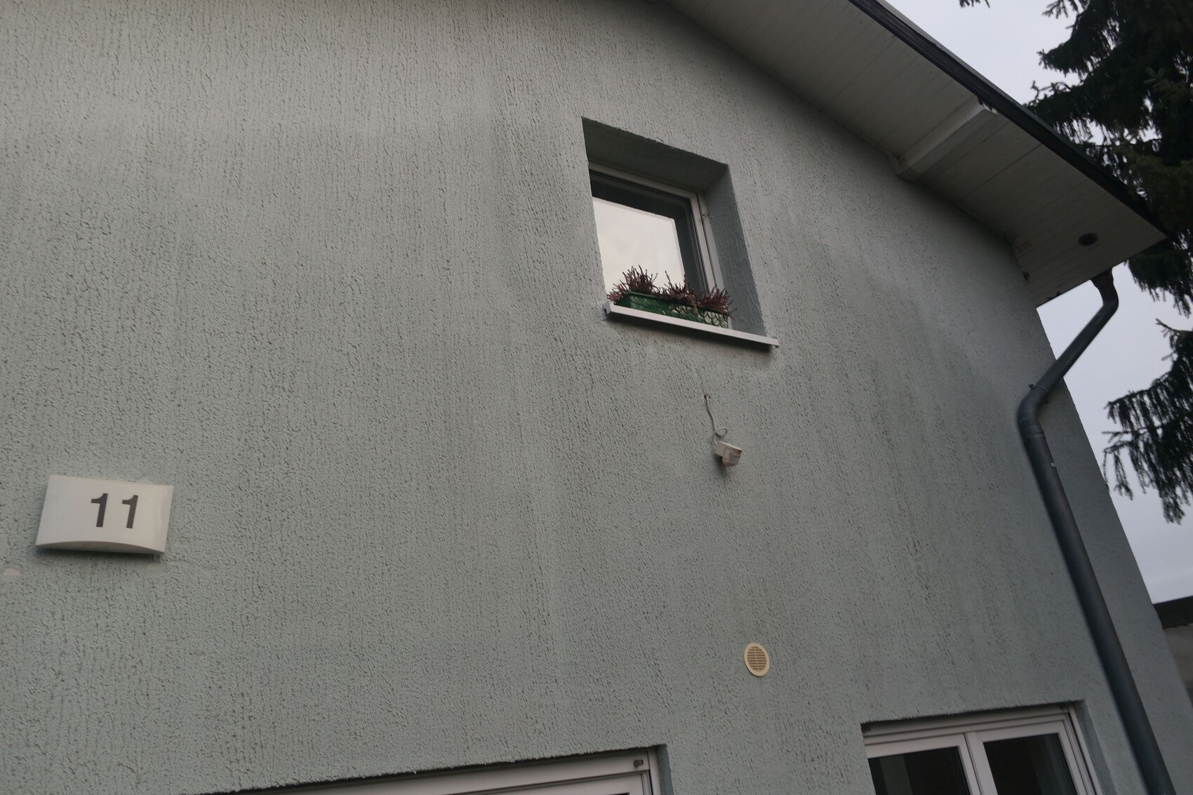 Außenwand eines Hauses mit kleinem Fenster und Blumenkasten, Hausnummer 11, Regenrohr rechts