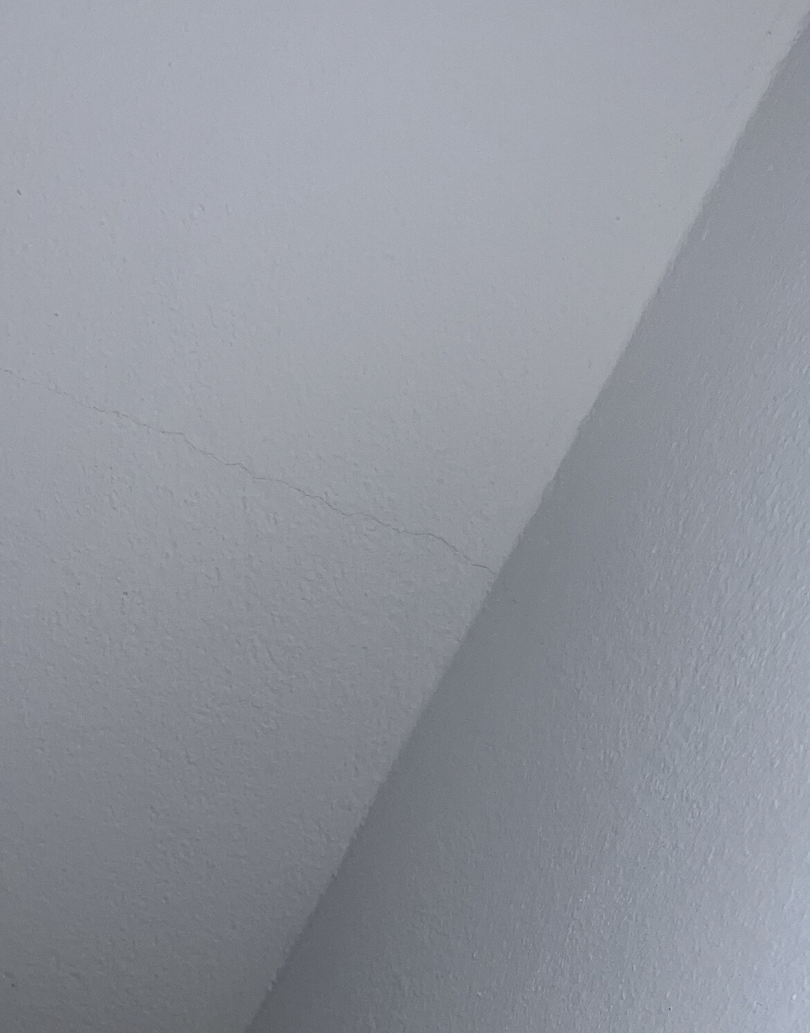 Weiße Innenwand-Ecke mit sichtbarer Risslinie und rauer Oberflächenstruktur.