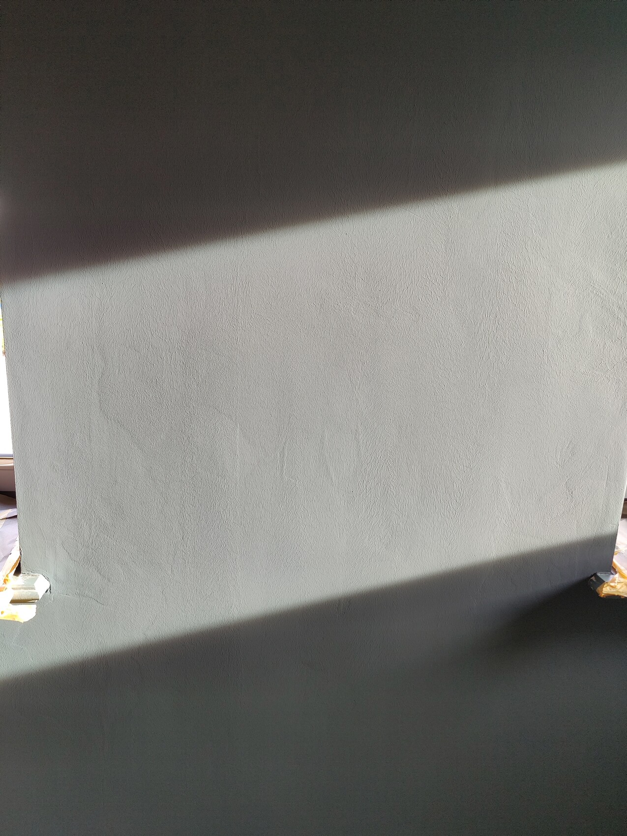 Grau verputzte Wand mit zwei diagonalen Schattenstreifen; Ecken mit Malerkrepp.