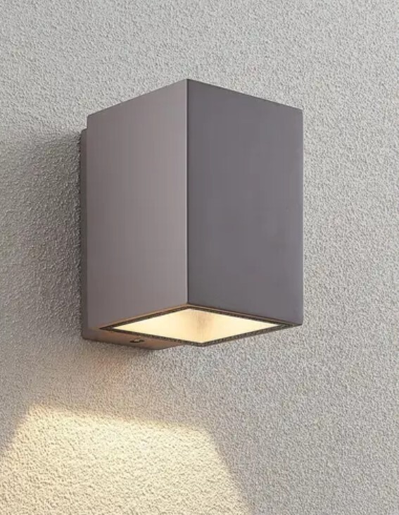 Außenwandleuchte in grauer quadratischer Kubusform, leuchtet nach unten an rauer Wand.