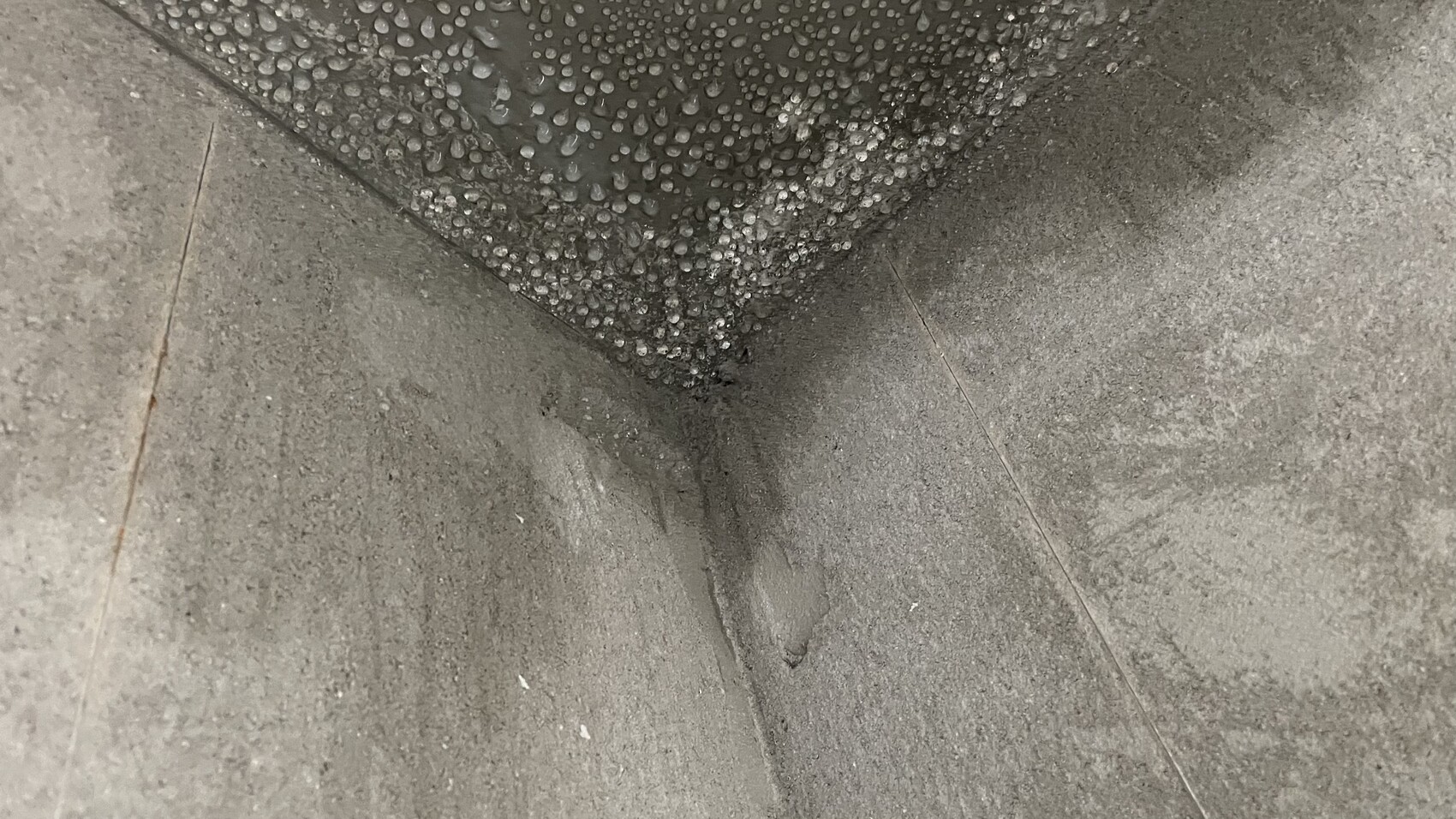 Ecke zweier Betonflächen; oben viele kleine Wassertropfen auf dunkler Oberfläche.