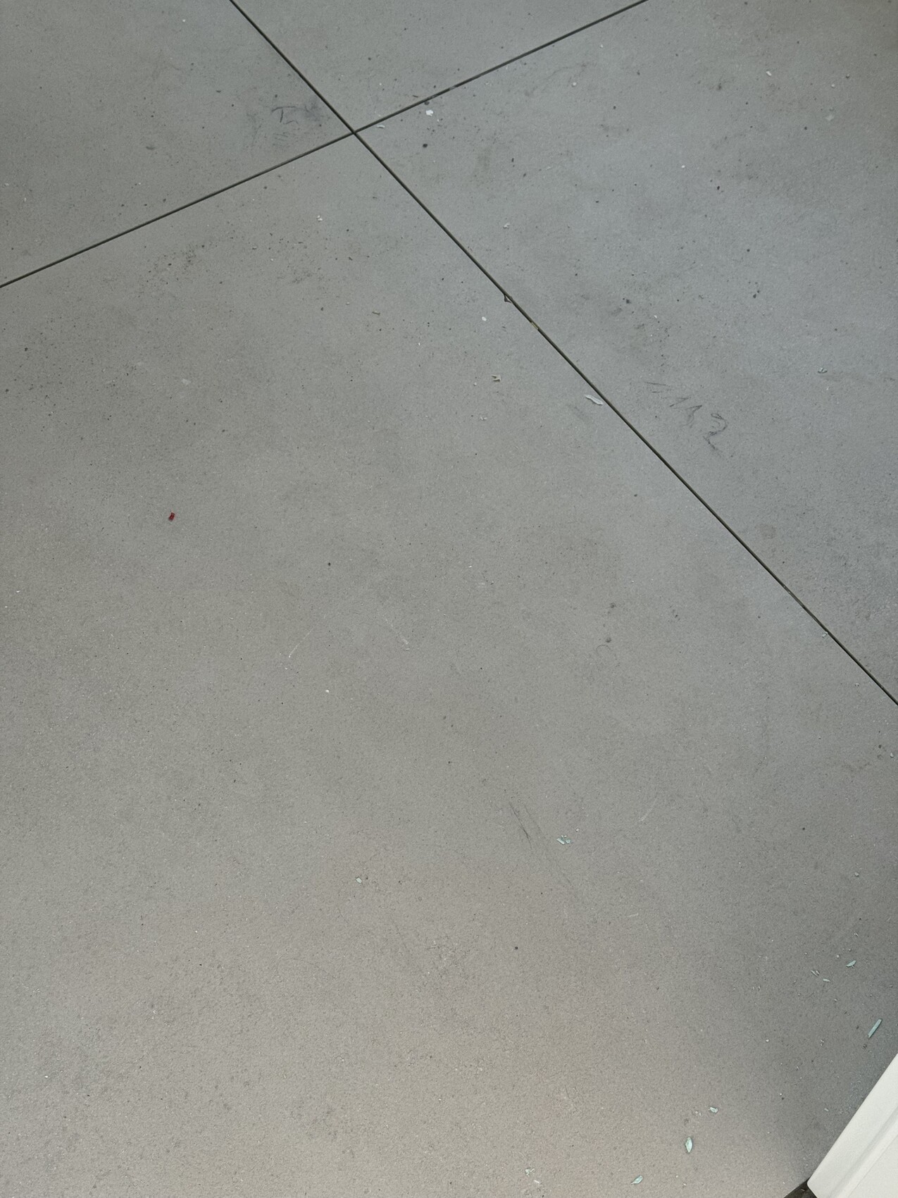 Hellgrauer Betonboden mit diagonalen Fugenlinien zwischen großen Platten, leicht verschmutzt.