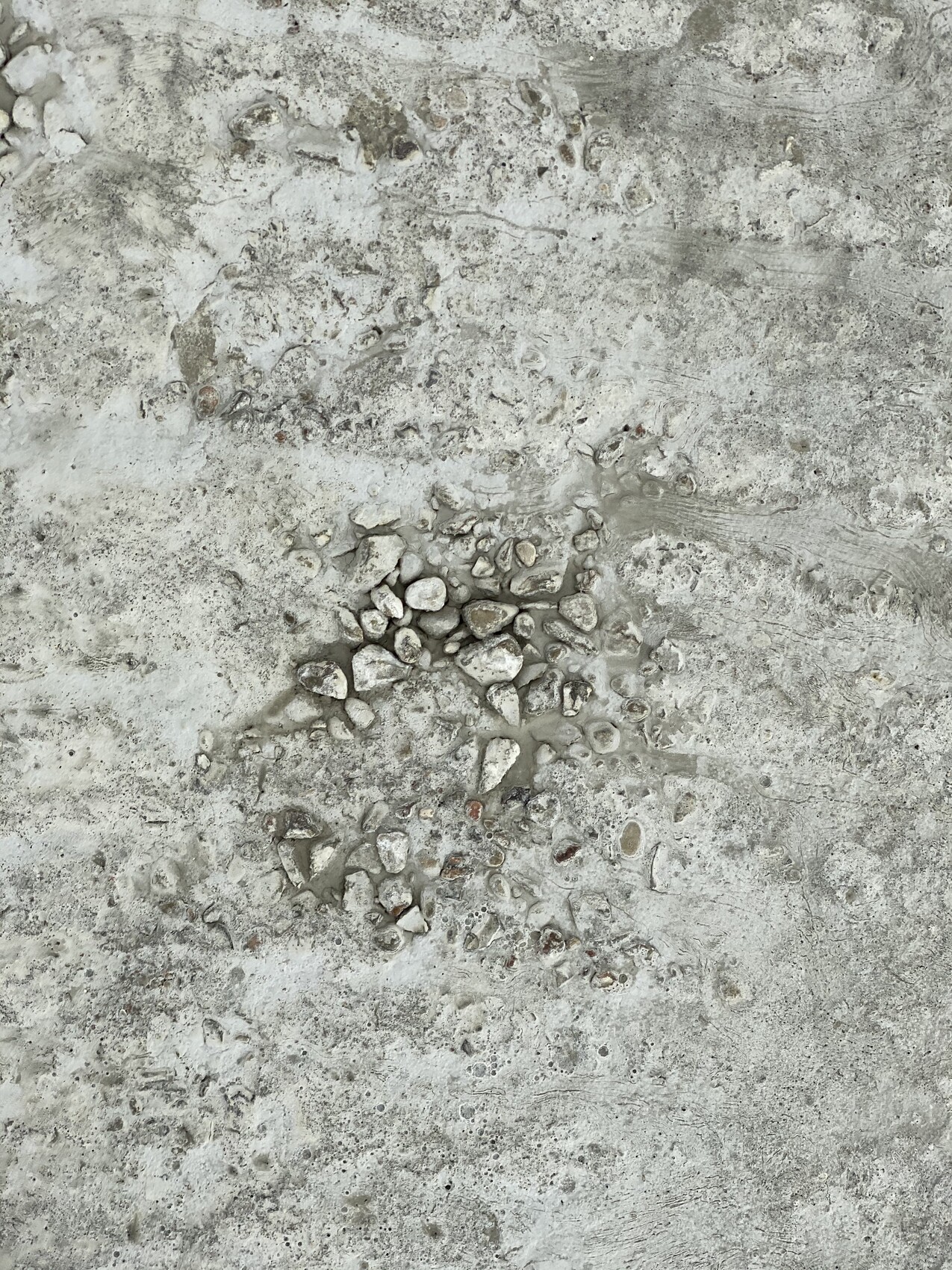 Graue Betonfläche mit zentraler Ansammlung kleiner Kieselsteine.