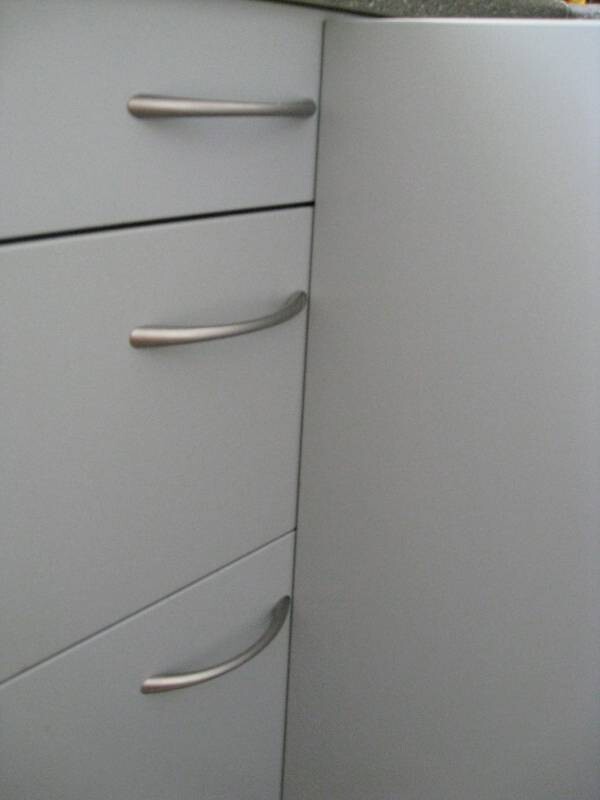 Grauer Küchenschrank mit drei Schubladen links und Tür rechts, silberne Griffe