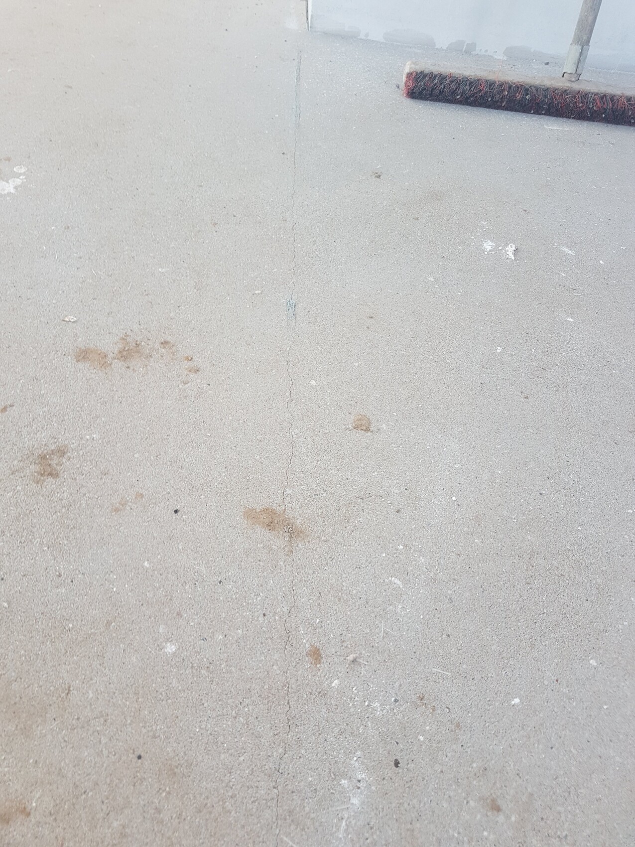 Glatte Betonfläche mit langer Mittelfuge, braune Flecken, Besen am oberen Rand.