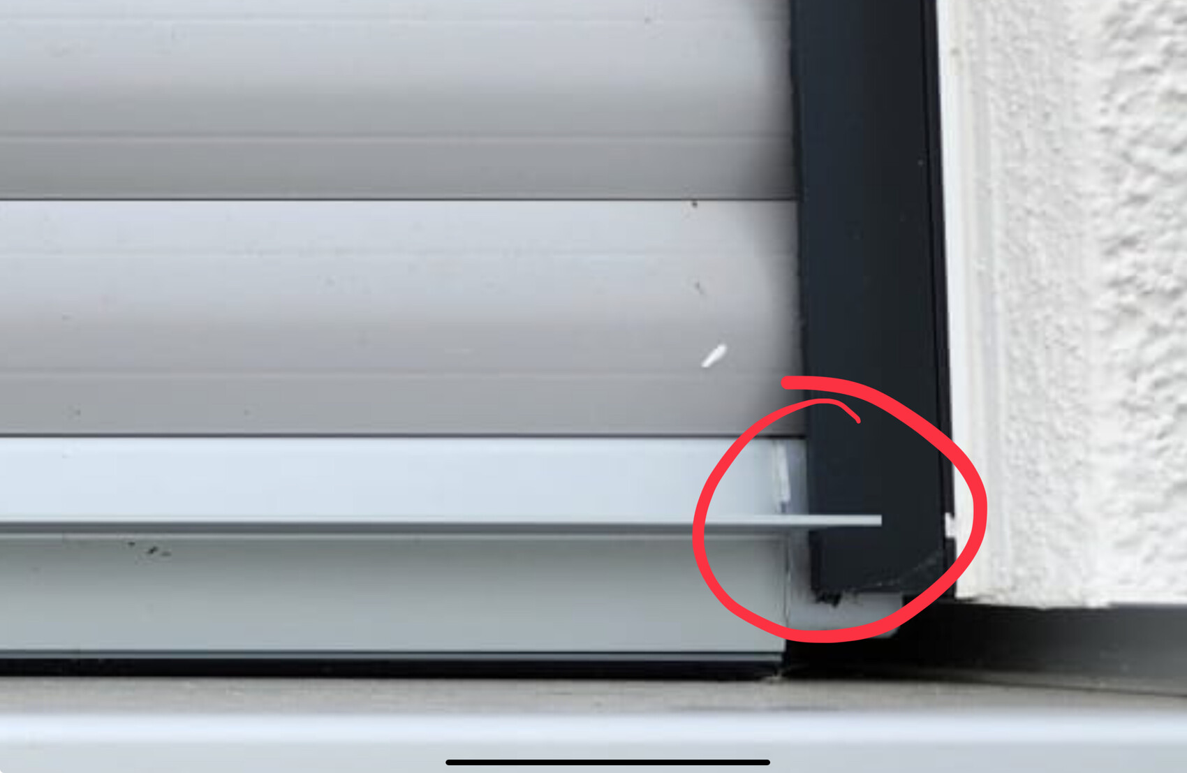 Nahaufnahme eines Rollladens mit einer weißen Stange, die horizontal in den unteren Spalt ragt.