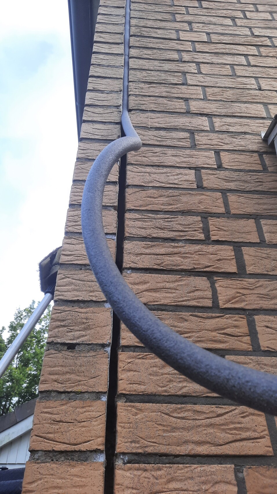 Graues Regenrohr mit Bogen an braunem Ziegelhaus, Außenansicht.