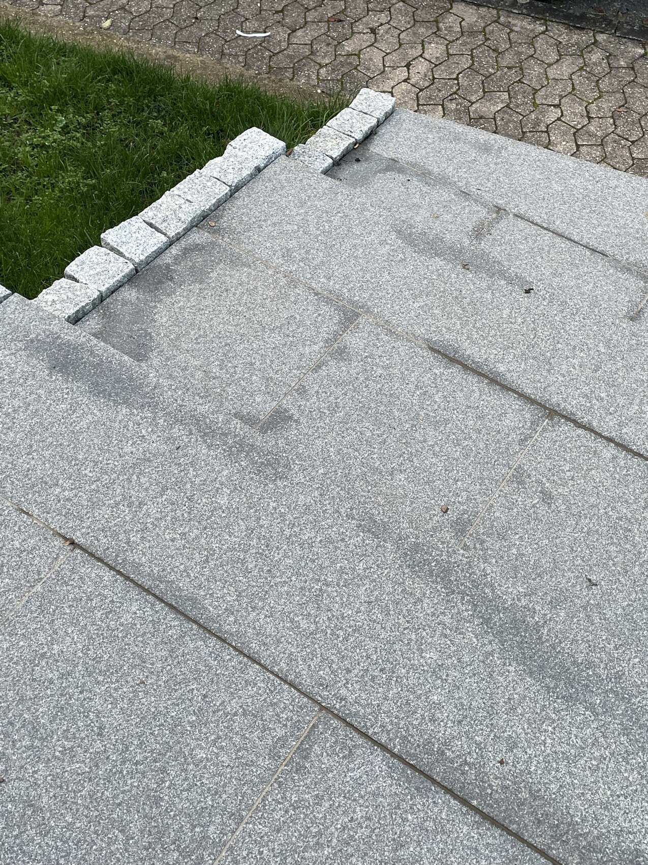 Draufsicht: graue Dachfläche mit kleinem Steinrand, Gras links, gepflasterter Weg dahinter
